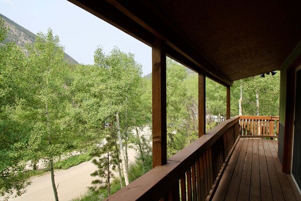 Una terraza de madera con vistas a un área boscosa y una montaña al fondo.