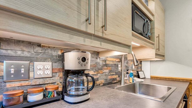 Cozinha moderna com backsplash de pedra, cafeteira, micro-ondas e pia de aço inoxidável.