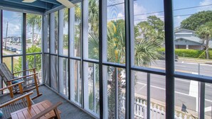 A room with large windows, a ceiling fan, wicker furniture, and a view of the street and greenery outside. - Marooned Mariner, Tybee Island (TYBEE ISLAND)