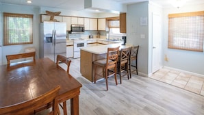 A modern kitchen with a central island, white cabinetry, stainless steel appliances, and wooden chairs. - Marooned Mariner, Tybee Island (TYBEE ISLAND)