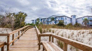 Una passerella in legno conduce a un hotel sulla spiaggia, dotato di numerosi balconi e una torre dell'orologio.