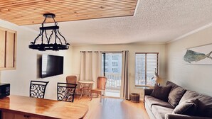Un soggiorno moderno con soffitto in legno, una televisione a schermo piatto, un divano, un tavolo da pranzo e un balcone con vista.