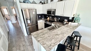 A modern kitchen with white cabinets, stainless steel appliances, and a granite countertop. - Makin' Memories South Beach~OceanView 3 queen beds (Tybee Island)