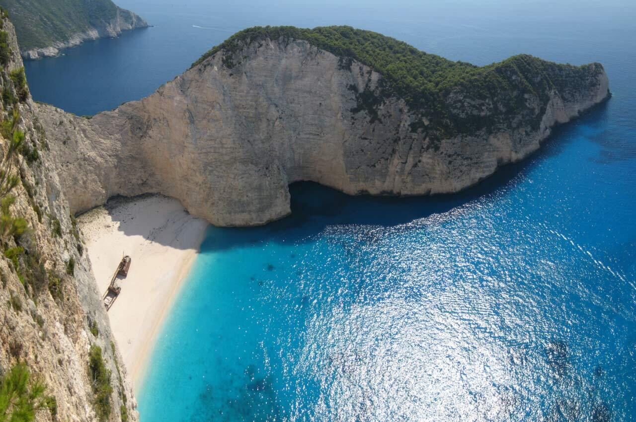 A coastal cliff with a beach and clear blue waters.