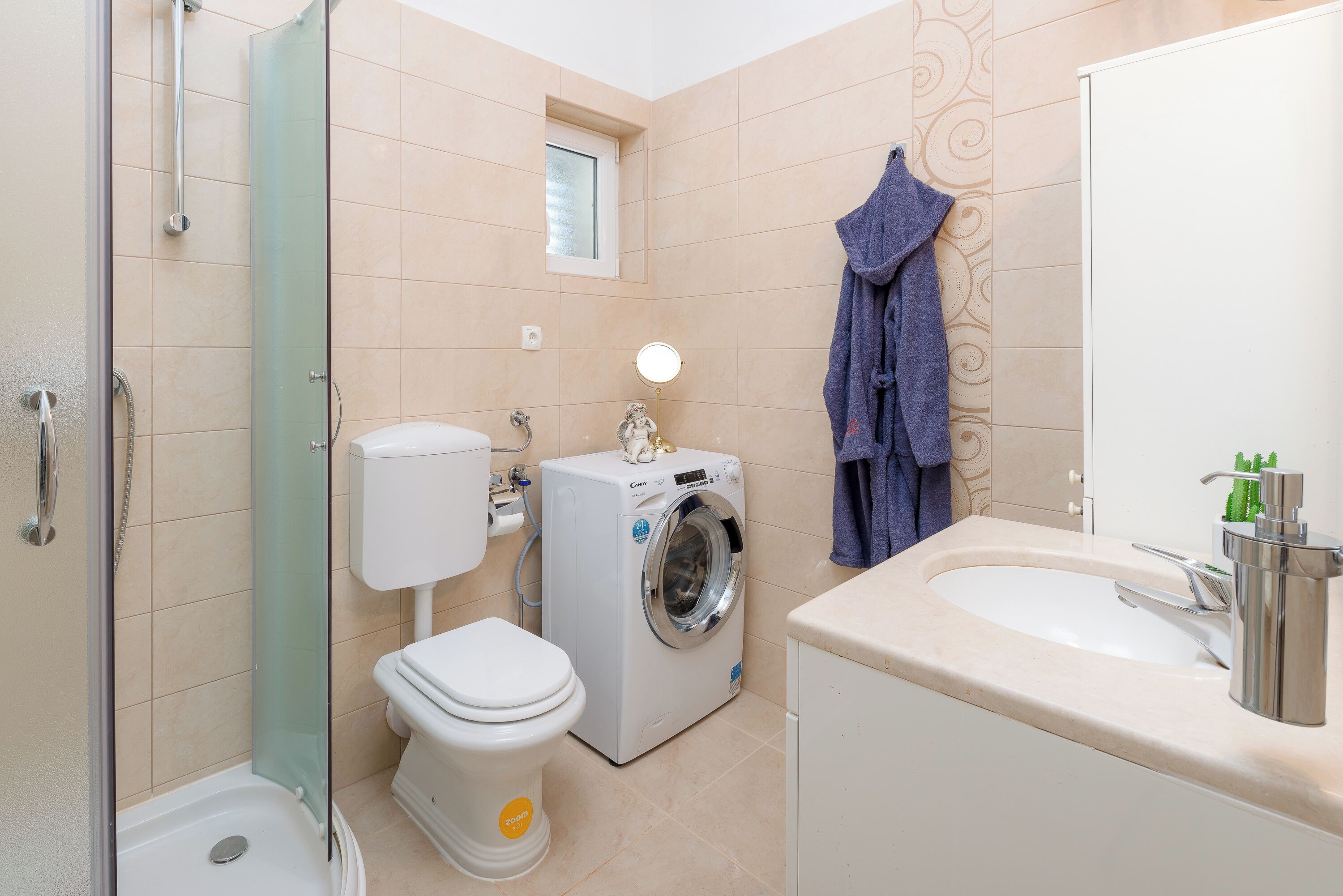 Une salle de bain compacte dotée d’une douche à parois de verre, d’un lave-linge, de toilettes et d’un lavabo avec un miroir.