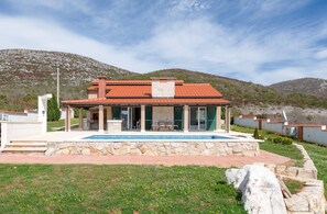 A two-story house with a red-tiled roof, a stone foundation, and a patio area with a table and chairs. - Villa Dea (Vučevica)