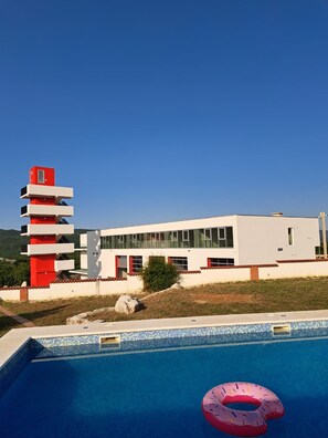 A modern building with a pool and a red and white structure nearby. - Villa Dea (Vučevica)