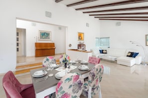 A dining area with a table set for four, a pink chair, and a white sofa in the background. - Villa Dea (Vučevica)