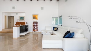 A modern living room with a white sofa, a TV on a stand, and a piano.