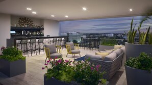 Eine Dachterrasse mit Stadtblick, modernen Sitzgelegenheiten und einer Bar mit einer Auswahl an Flaschen.