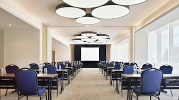 A conference room with rows of tables and chairs, a carpeted floor, and a modern ceiling light fixture.