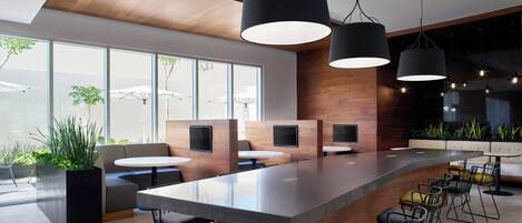 A modern bar area with a long counter, multiple seating options, and large pendant lights.