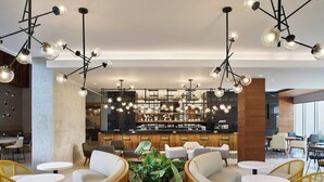 Ein stilvoller Lounge-Bereich mit runden Tischen, bequemen Sitzgelegenheiten und einer Bar im Hintergrund.