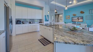 A modern kitchen with white cabinets, a granite countertop, and pendant lighting. - Pelican Shores | 2 King Suites | Pool | Jacuzzi | Lounge (Rotonda West)
