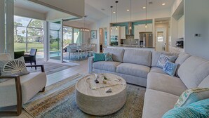 A spacious living area with a large sofa, a coffee table, and a view of the outdoors through large glass doors. - Pelican Shores | 2 King Suites | Pool | Jacuzzi | Lounge (Rotonda West)