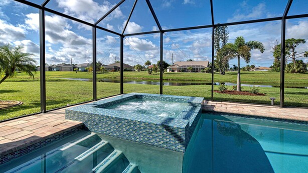 A pool with a hot tub, surrounded by a glass enclosure with a view of a grassy area and houses. - Pelican Shores | 2 King Suites | Pool | Jacuzzi | Lounge (Rotonda West)