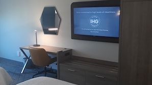 A hotel room with a bed, a desk, a chair, a TV displaying a cleanliness commitment, and a wardrobe. - Holiday Inn Express & Suites Jackson by IHG (Jackson)