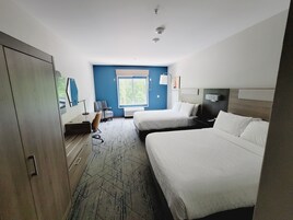 Habitación de hotel con dos camas, un escritorio, una silla y una ventana con vista a follaje.