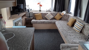 A compact living space with a sofa, a television, a small table, and a window with curtains. - 2 bed Caravan Approx 10 Mins From Beach Suzie 2 (Hull)