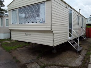 A mobile home with a sliding door, a window with a decorative curtain, and a small set of steps leading to the door.
