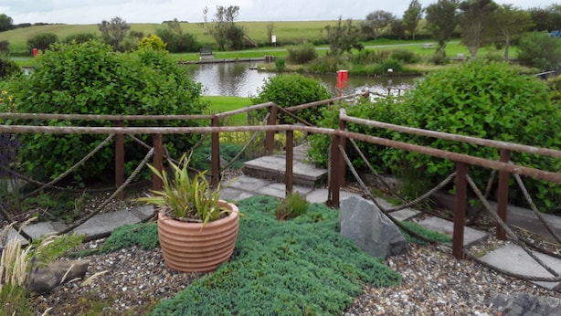 A rustic wooden bridge over a pond, surrounded by lush greenery and a distant view of a park. - 2 bed Caravan Approx 10 Mins From Beach Suzie 2 (Hull)