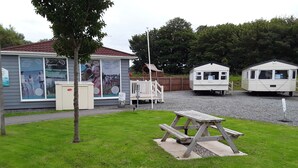 A campsite with a picnic table, a small building with a sign, and a fenced area. - 2 bed Caravan Approx 10 Mins From Beach Suzie 2 (Hull)