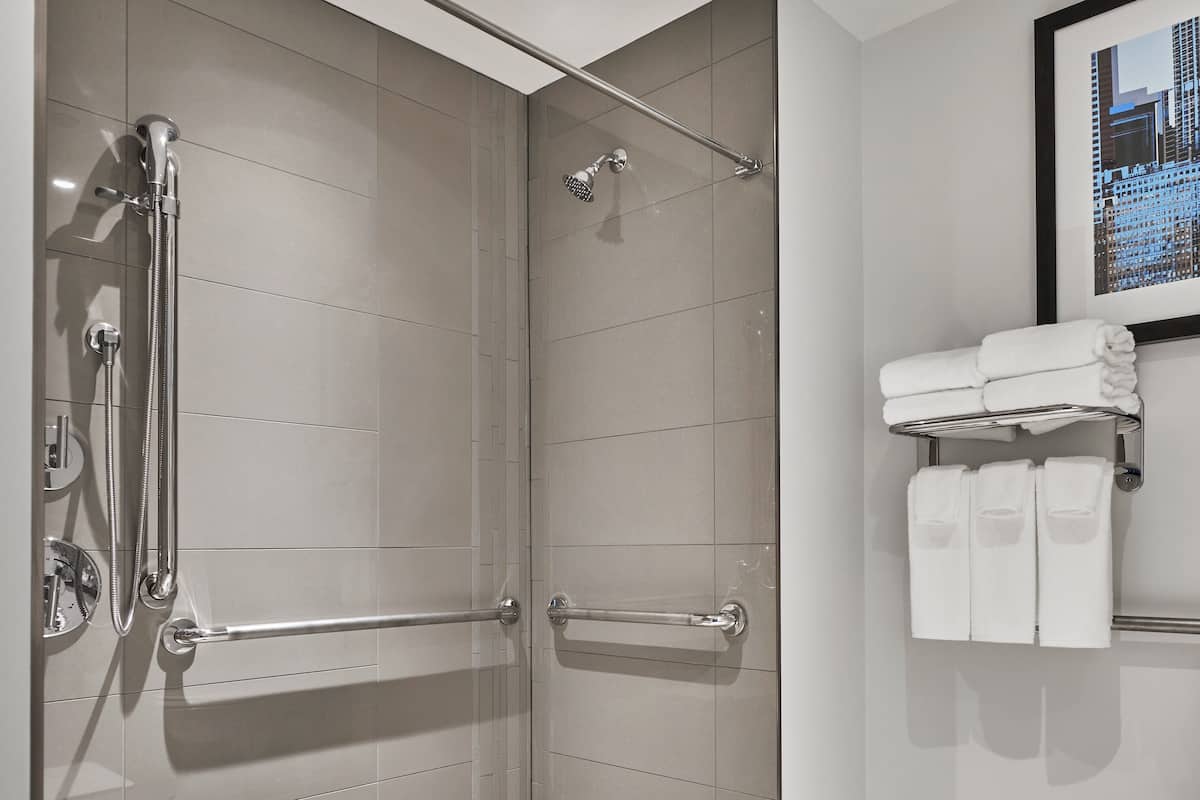 Un baño moderno con cabina de ducha a ras de suelo, barras de apoyo, inodoro con asiento de seguridad y toallero con toallas dobladas con cuidado.