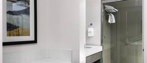 A modern bathroom with a glass shower, a white sink, and a framed artwork on the wall.