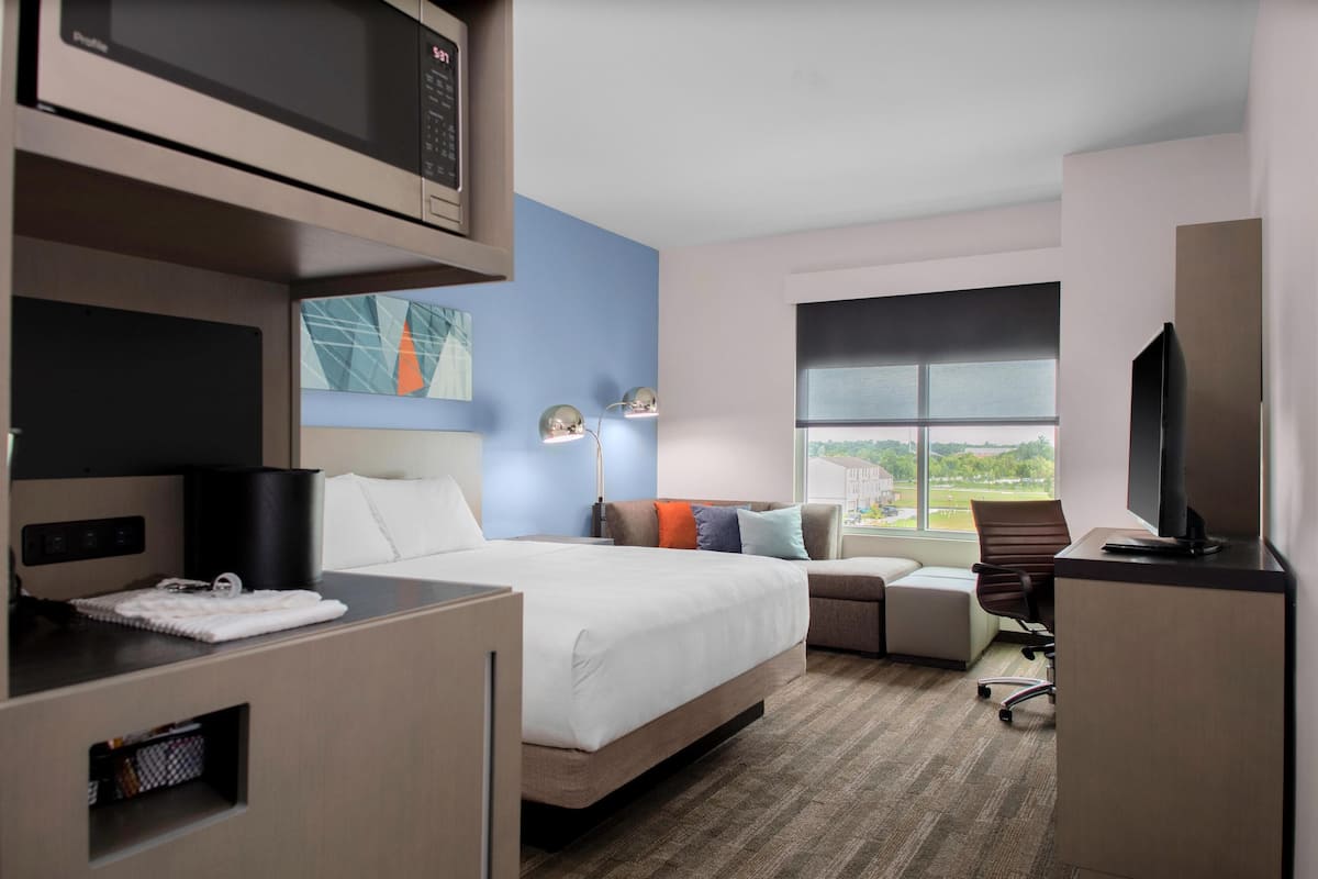 Habitación de hotel con cama, escritorio, televisión, lámpara y ventana con vistas.
