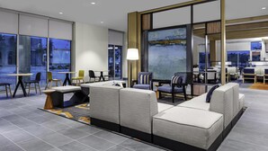 Een moderne hotel lobby met een zithoek, een groot raam en uitzicht op buiten.