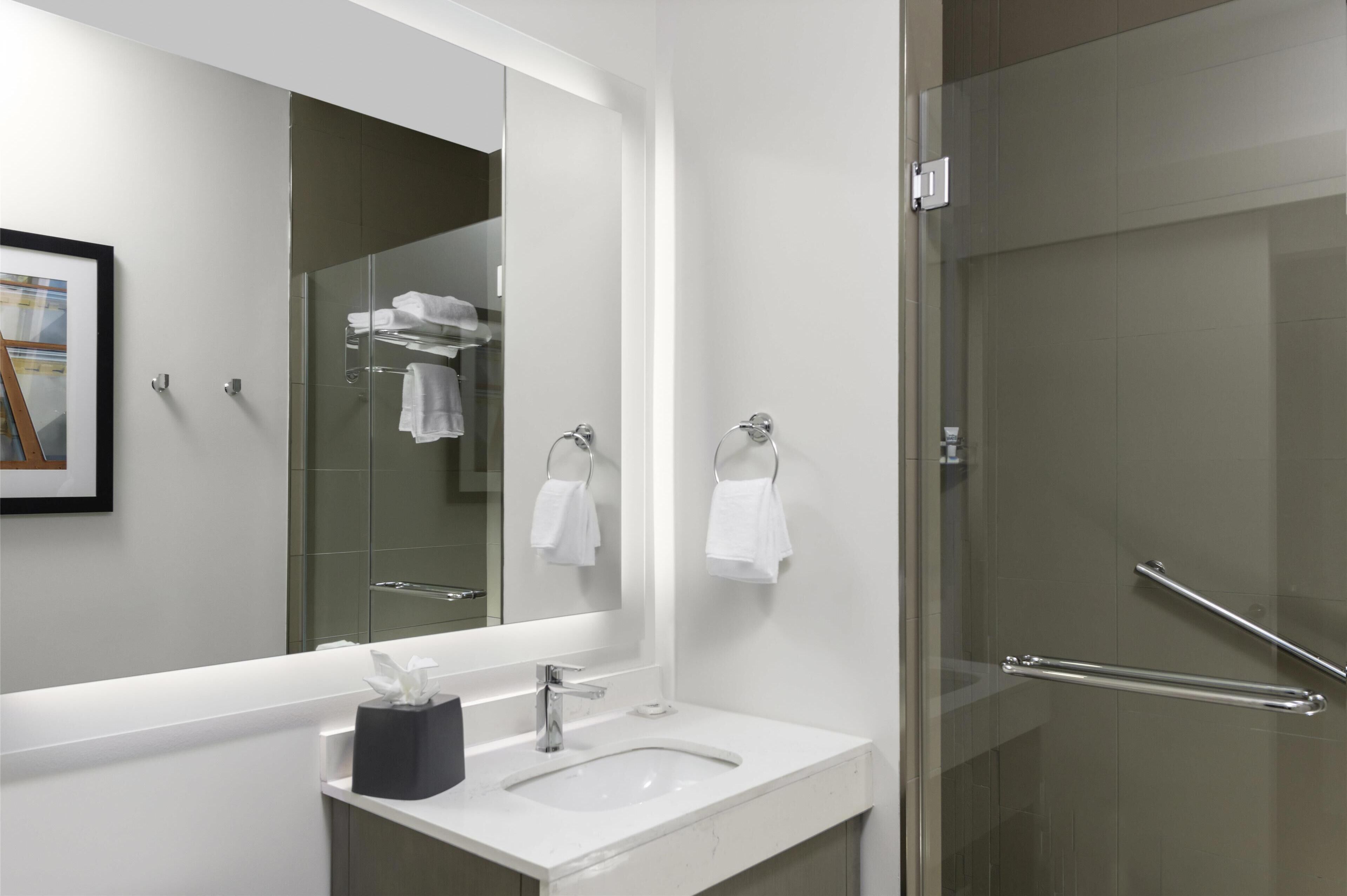 A modern bathroom with a large mirror, a sink, a glass shower enclosure, and towel hooks.