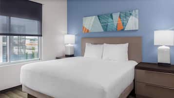 Quarto de hotel com uma cama grande, duas mesas de cabeceira com abajures, uma janela com persianas e vista para a cidade.