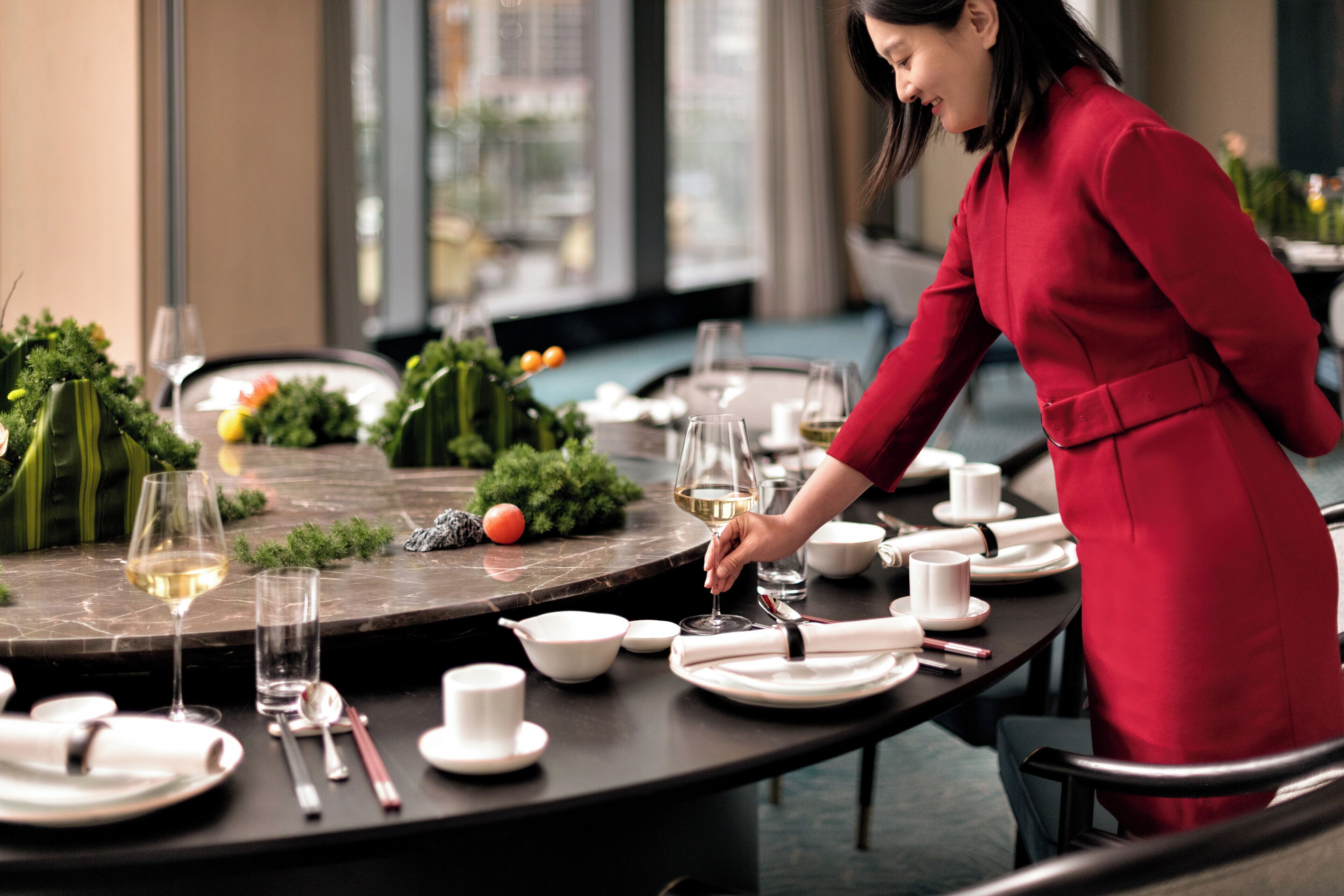 A well-set dining table with white plates, bowls, and cutlery, and a glass of white wine.