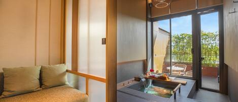 Una habitación japonesa tradicional con suelo de tatami, una mesa baja de madera y un puertas correderas que dan a un área exterior con vistas a zonas verdes.