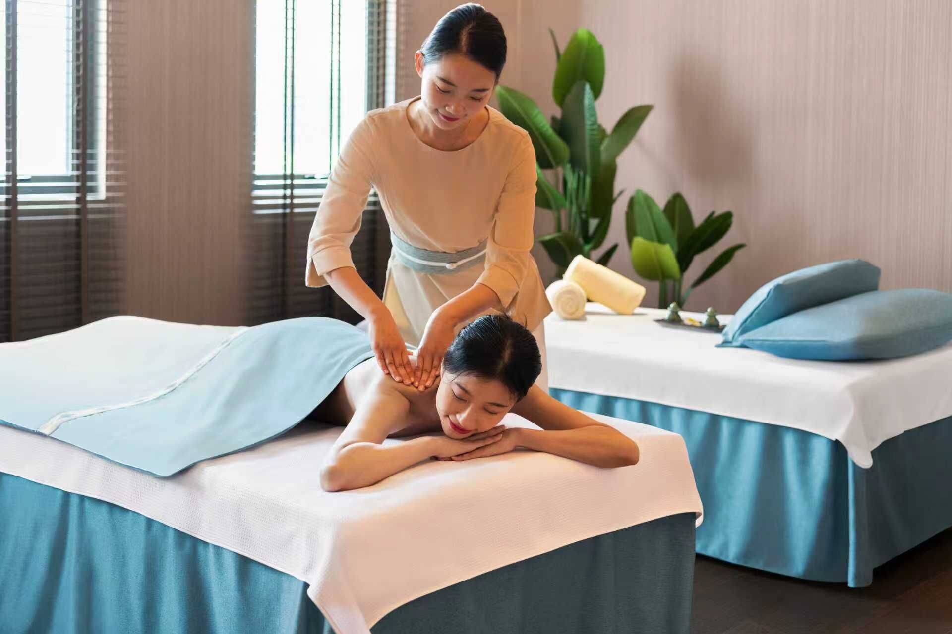 Una seduta di massoterapia in una spa con lettino, tavolo da massaggio e un piccolo tavolo con asciugamani e una pianta.