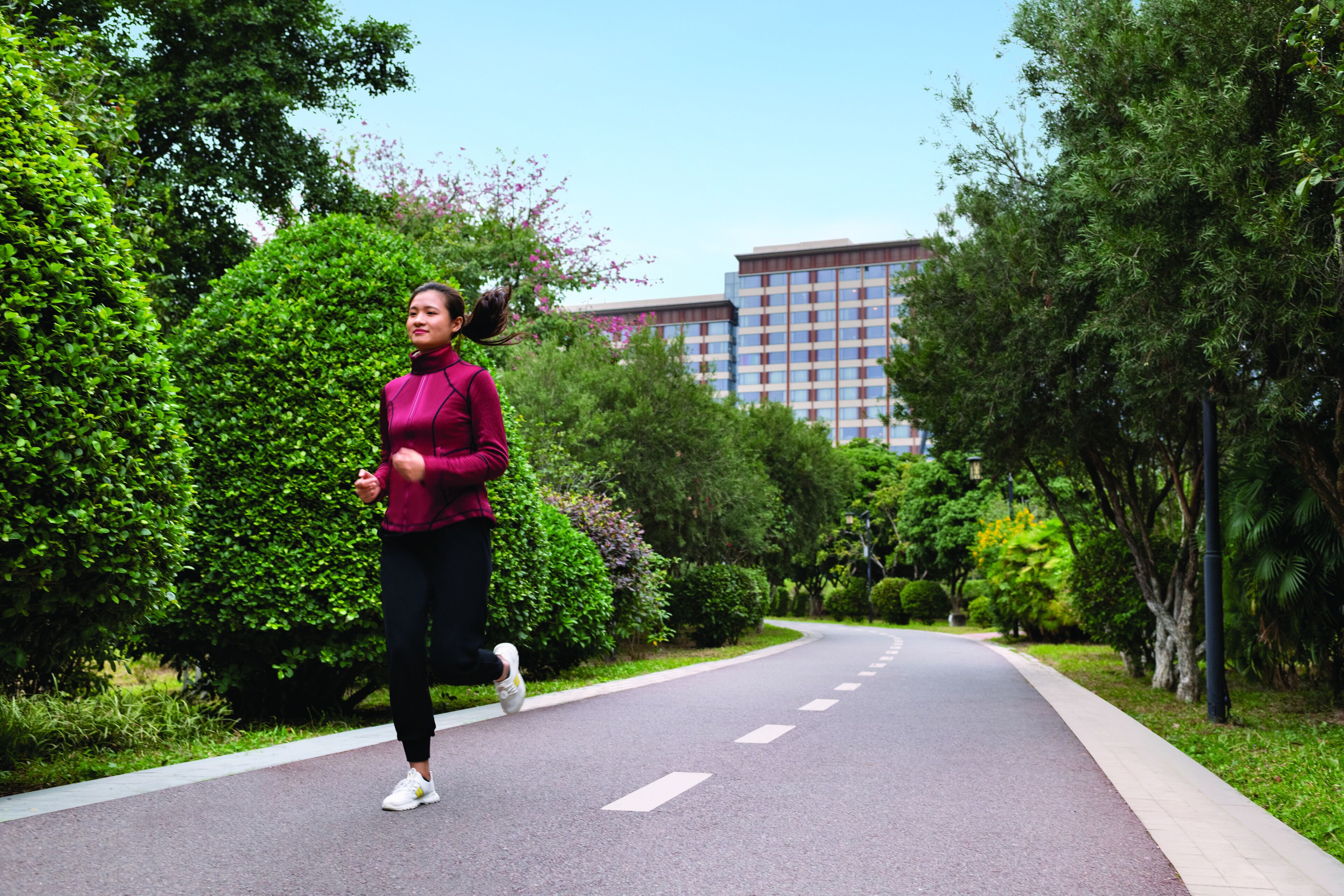 Una donna corre su un sentiero alberato, con un edificio sullo sfondo.