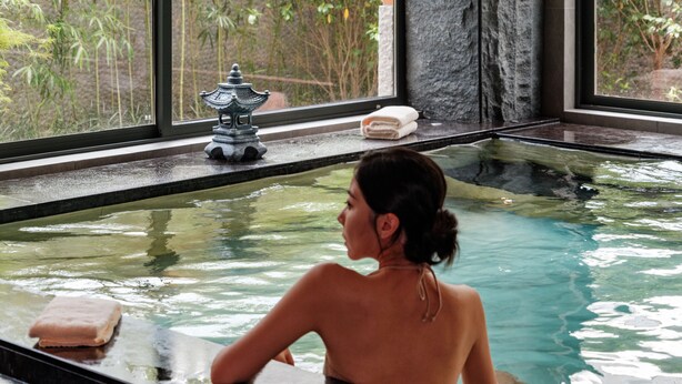 Una persona en una bañera con vista a un bosque de bambú.