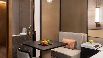 A modern hotel room with a marble bathroom, a small dining table with fruit, a sofa, and a nightstand with a lamp.