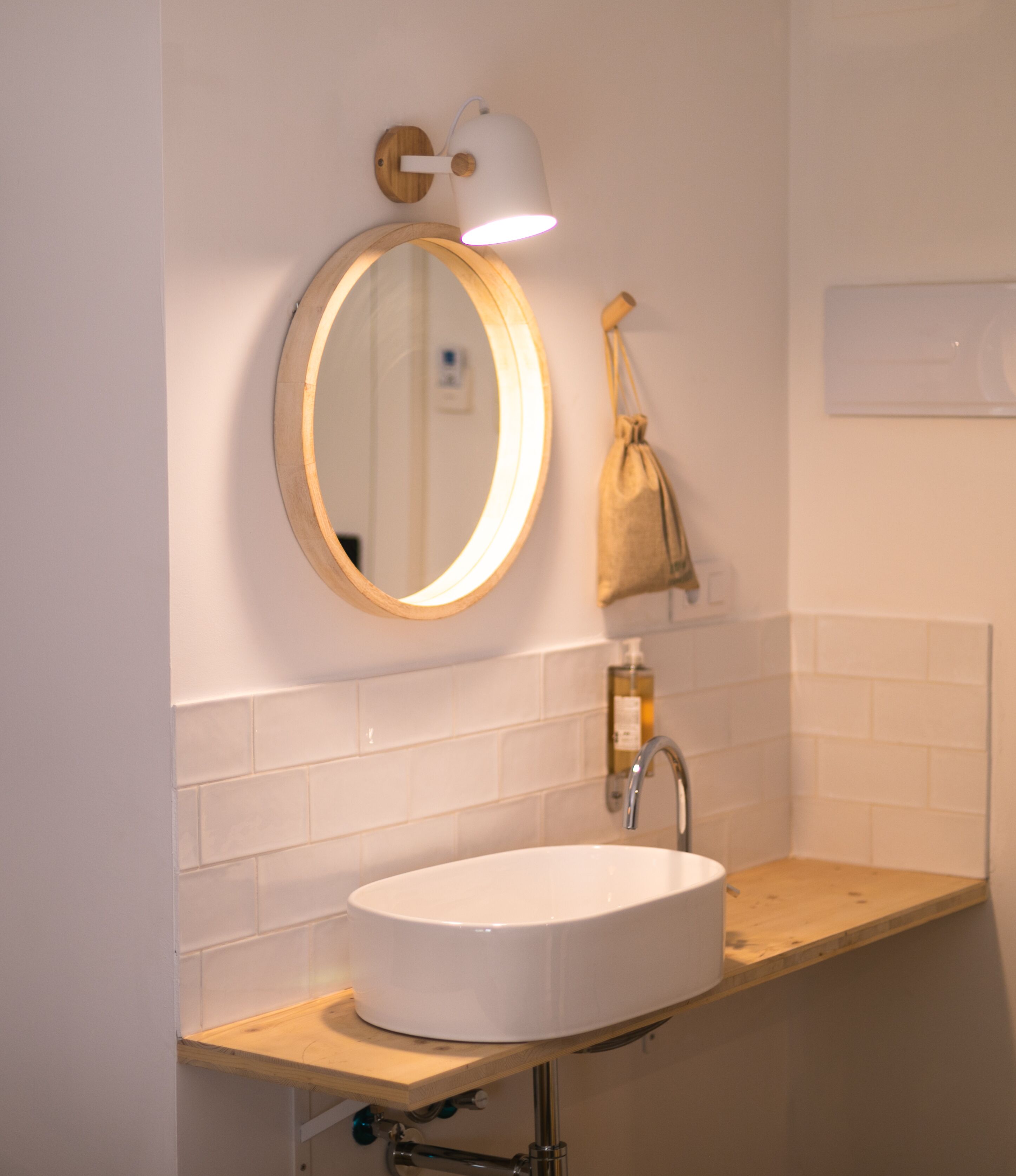 A bathroom with a round mirror, a white sink, a towel hanging on the wall, and a small wooden shelf.