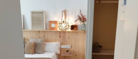 Une chambre confortable avec une tête de lit en bois, un lit recouvert de draps blancs, une table de chevet et un luminaire suspendu.