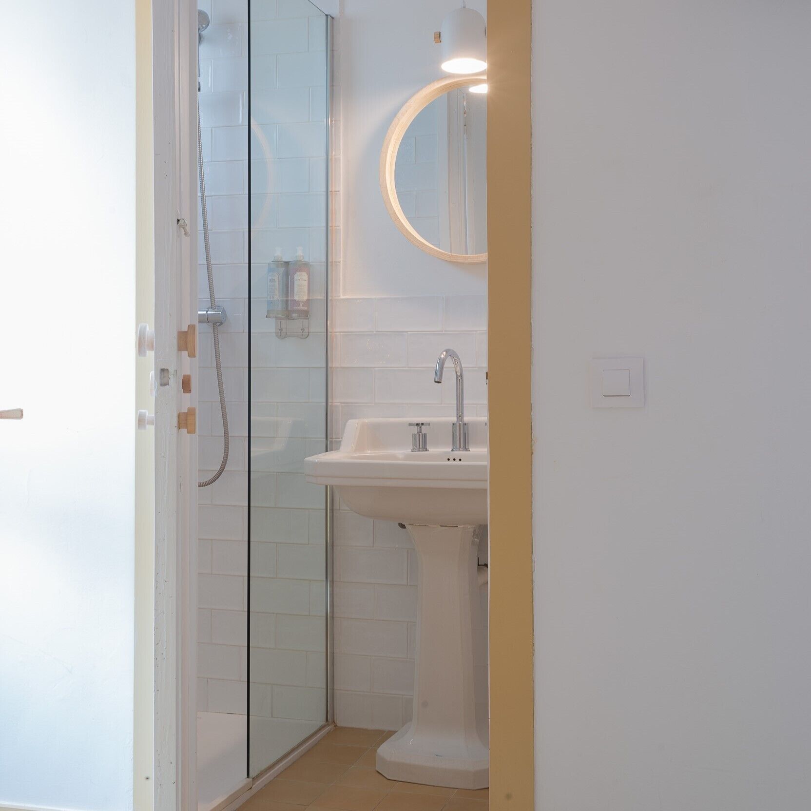 A bathroom with a glass shower enclosure, a pedestal sink, and a mirror with a wooden frame.