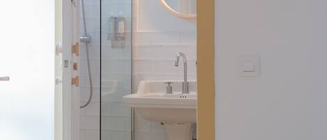 A bathroom with a glass shower enclosure, a pedestal sink, and a mirror with a wooden frame.
