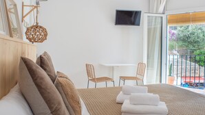 A hotel room with a bed, pillows, a TV, a small table, chairs, and a balcony with a view. - Hostal Sa Teula (Palafrugell)