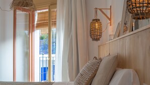 A bedroom with a bed, pillows, a woven headboard, a hanging light fixture, and a view of a balcony. - Hostal Sa Teula (Palafrugell)