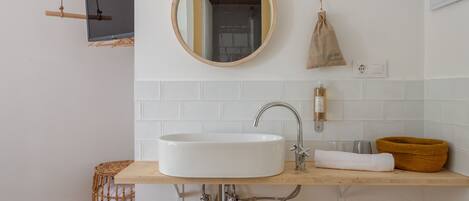 A bathroom with a round mirror, a white sink, a towel, and a small basket.