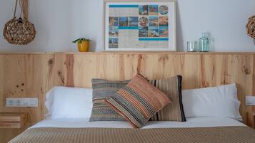 Una cama bien hecha con almohadones estampados, un collage enmarcado en la pared y una planta pequeña.
