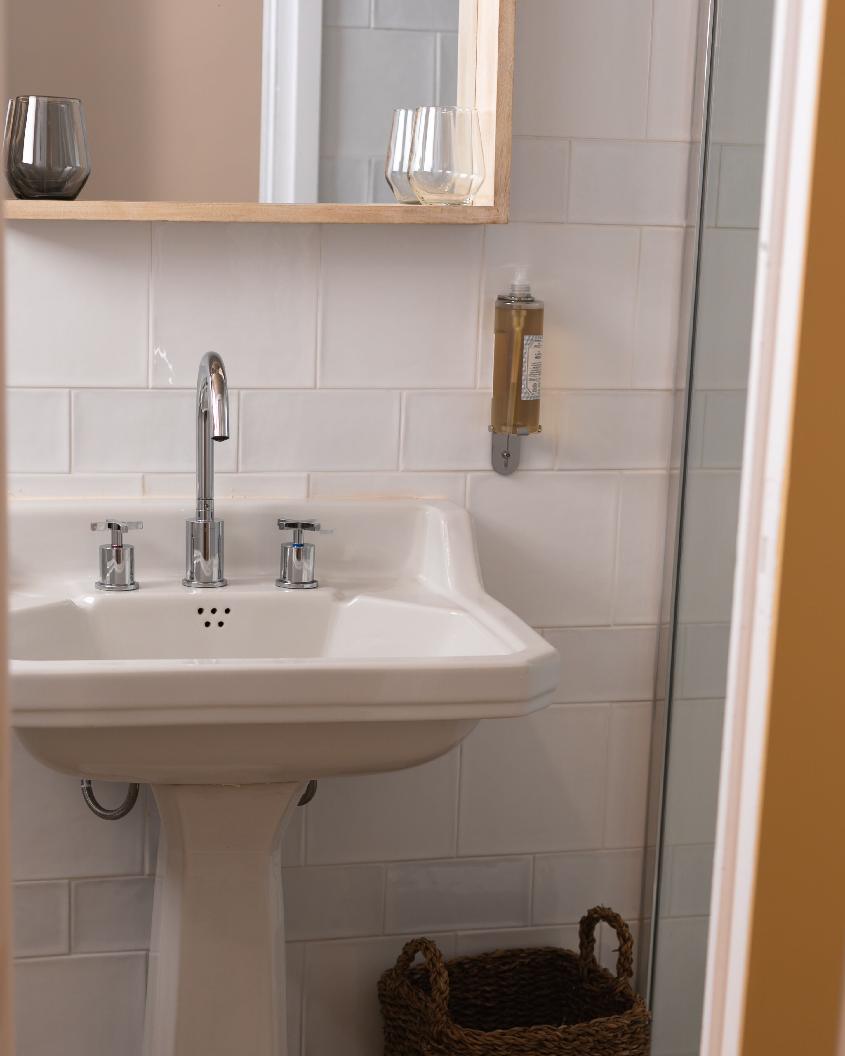 Un baño con un lavamanos blanco, dos grifos y un espejo encima.