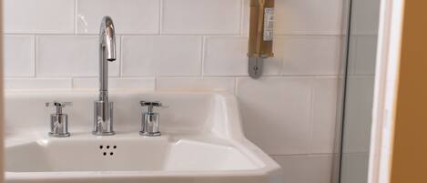Un baño con un lavamanos blanco, dos grifos y un espejo encima.