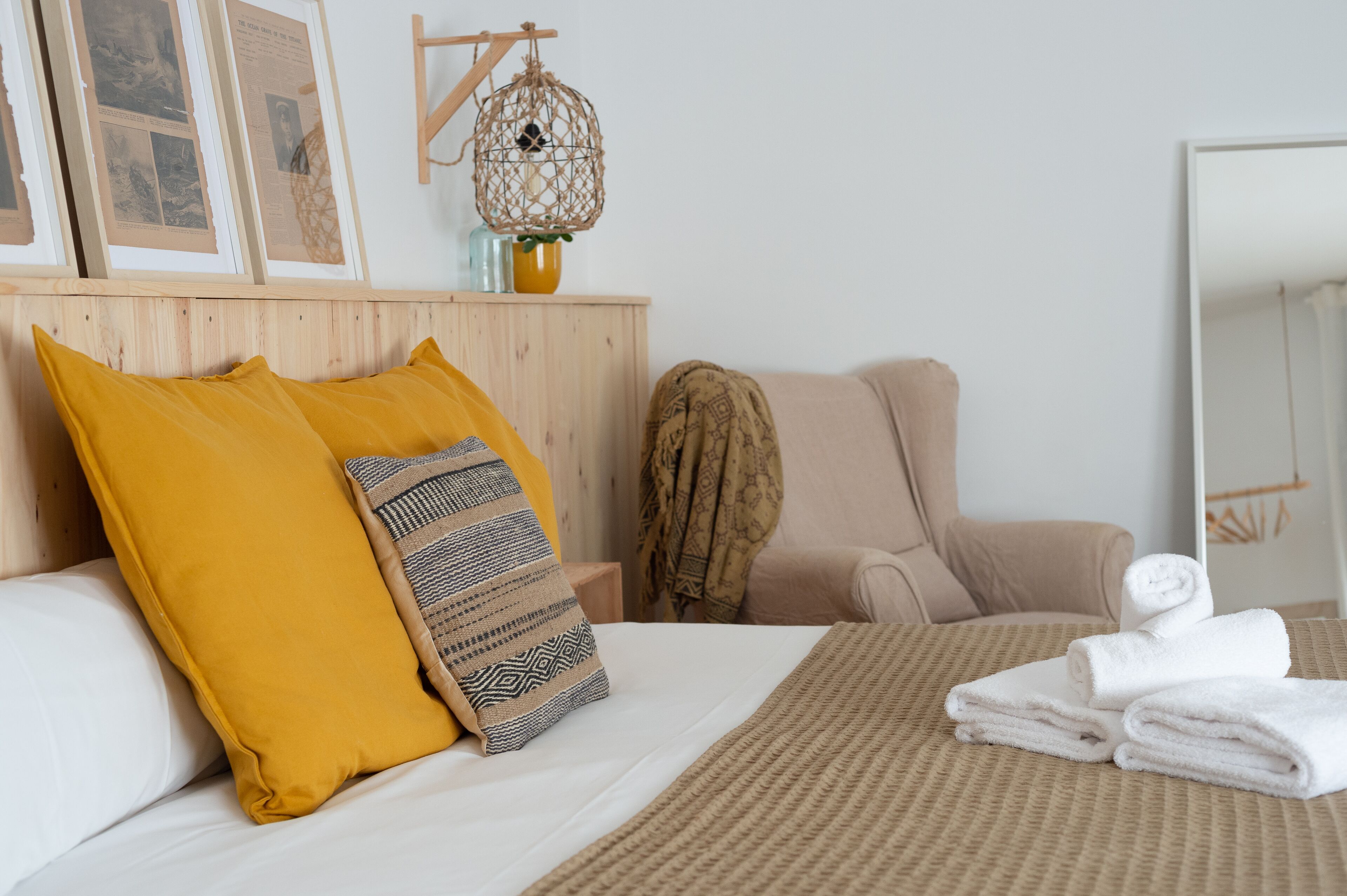 A neatly arranged hotel room with a bed, a chair, a mirror, and a wall with framed pictures.