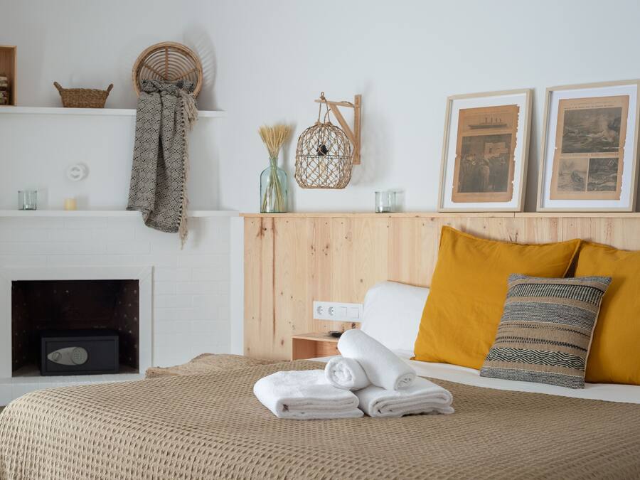 Un dormitorio ordenado con cama, almohadas, una mesita de noche, estante en la pared y chimenea.